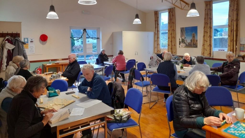 People sat around tables talking and playing board games in a community hall
